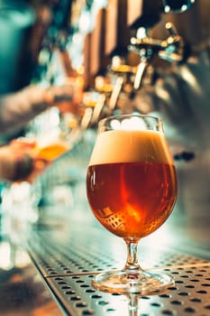 Hand of bartender pouring a large lager beer in tap. Soft, vintage instagram effect on photo. Pouring beer for client. Side view of young bartender pouring beer while standing at the bar counter