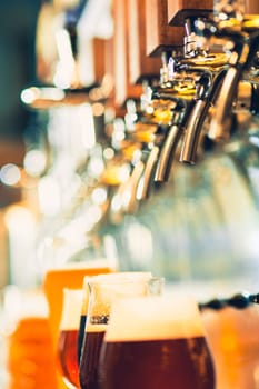 The beer taps in a pub. nobody. Selective focus. Alcohol concept. Vintage style. Beer craft. Bar table. Steel taps. Shiny taps. Glass of beer