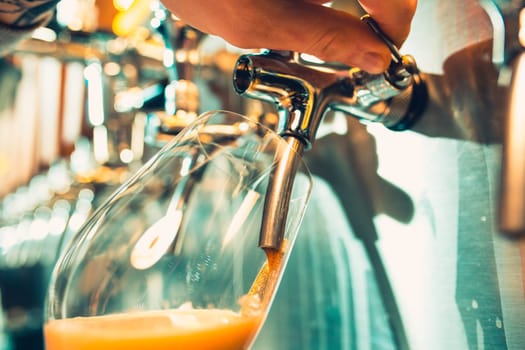 Hand of bartender pouring a large lager beer in tap. Soft, vintage instagram effect on photo. Pouring beer for client. Side view of young bartender pouring beer while standing at the bar counter