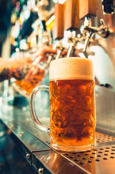 We meet oktoberfest. Hand of bartender pouring a large lager beer in tap. Pouring beer for client. Side view of young bartender pouring beer while standing at the bar counter