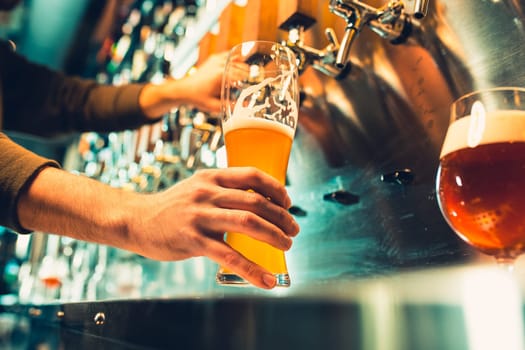 Hand of bartender pouring a large lager beer in tap. Soft, vintage instagram effect on photo. Pouring beer for client. Side view of young bartender pouring beer while standing at the bar counter