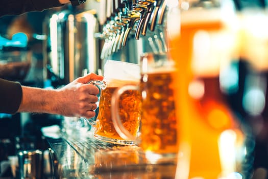 Hand of bartender pouring a large lager beer in tap. Soft, vintage instagram effect on photo. Pouring beer for client. Side view of young bartender pouring beer while standing at the bar counter