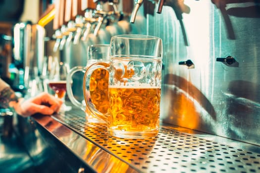 We meet oktoberfest. Hand of bartender pouring a large lager beer in tap. Pouring beer for client. Side view of young bartender pouring beer while standing at the bar counter