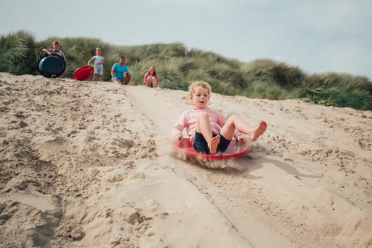 Little girl having fun, sliding down a sand dune while her family wait at the top.