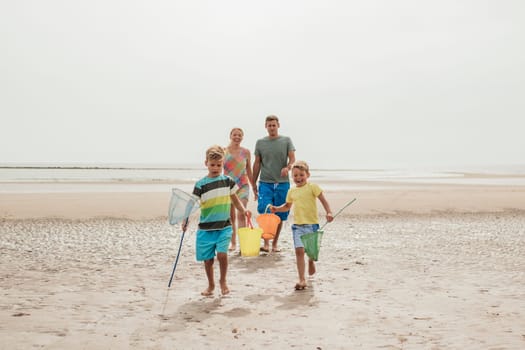 Front view of family walking up the beach with buckets and fishing nets.
