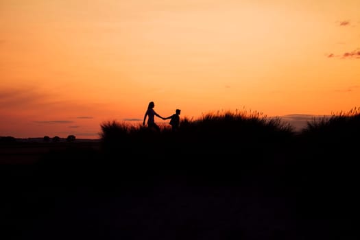 Silhouette of a mother and son walking through the sand dunes at sunset.