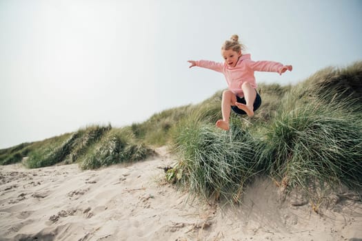 Little girl jumping over a sand dune while on holiday with her family, having some fun.