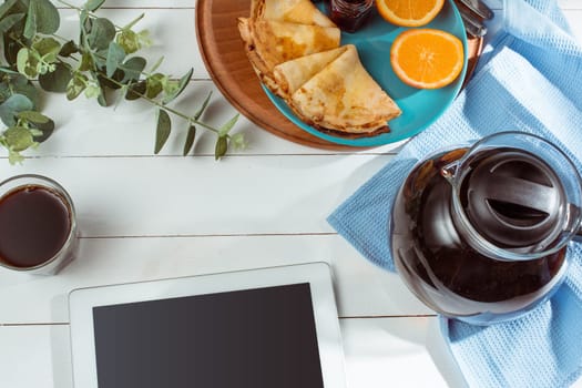 The tablet and pancakes with juice. Healthy breakfast. Fresh homemade french crepes made with ffresh fruits on a vintage wooden board on the wooden table. Top view with with honey, fruits and coffee. French pancakes concept