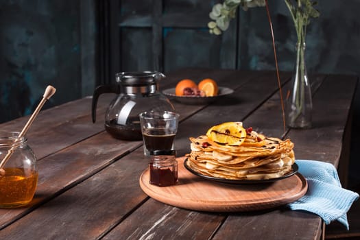 Fresh homemade french crepes made with ffresh fruits on a vintage wooden board on the wooden table. Side view with honey, fruits and coffee. French pancakes concept