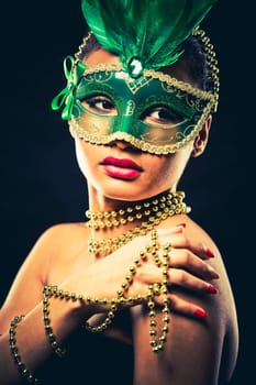Upscale Indian woman wearing gold jewellery and red lipstick on black background. Green party mask.