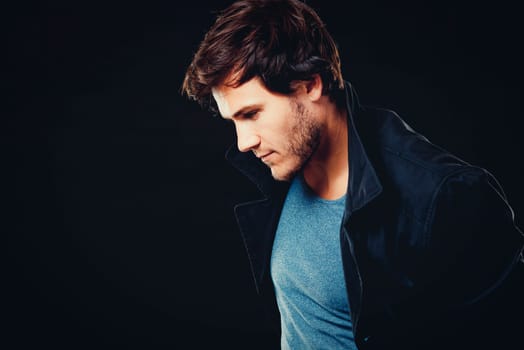 Close-up face of young bearded man on dark background modern and dramatic photo. Caucausian male model is wearing blue tshirt and black jacket.