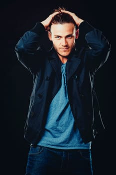 Close-up face of young bearded man on dark background modern and dramatic photo. Caucausian male model is wearing blue tshirt and black jacket.