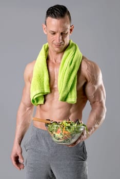 Powerful athletic man with great physique eating a healthy salad.