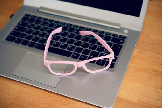 laptop with pink glasses on wooden ground