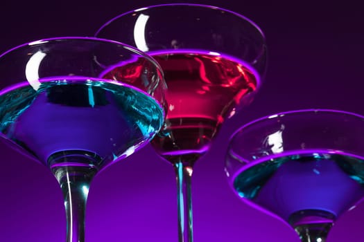 Three wine stuffed glasses standing on the table at studio. Vivid bright colored lighting. Trendy in 2018 Ultra Violet Light Bulb. Art decoration with tone of mystic color