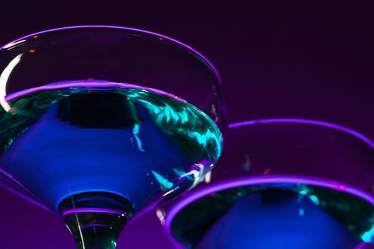 Two wine stuffed glasses standing on the table at studio. Vivid bright colored lighting. Trendy in 2018 Ultra Violet Light Bulb. Art decoration with tone of mystic color