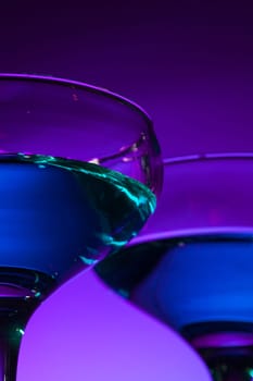 Two wine stuffed glasses standing on the table at studio. Vivid bright colored lighting. Trendy in 2018 Ultra Violet Light Bulb. Art decoration with tone of mystic color