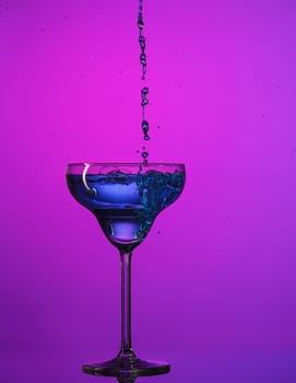 The wine stuffed glasse with cocktail standing on the table at studio. Vivid bright colored lighting. Trendy in 2018 Ultra Violet Light Bulb. Art decoration with tone of mystic color