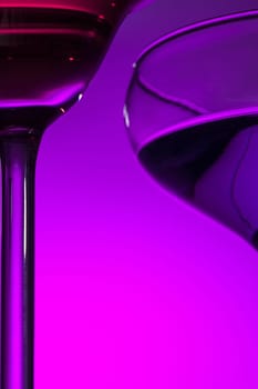 Two wine stuffed glasses standing on the table at studio. Vivid bright colored lighting. Trendy in 2018 Ultra Violet Light Bulb. Art decoration with tone of mystic color