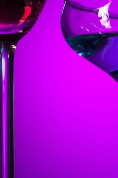 Two wine stuffed glasses standing on the table at studio. Vivid bright colored lighting. Trendy in 2018 Ultra Violet Light Bulb. Art decoration with tone of mystic color