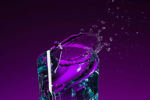 The water splashing in glass on lilac background at studio. Vivid bright colored lighting. Trendy in 2018 Ultra Violet Light Bulb. Art decoration with tone of mystic color