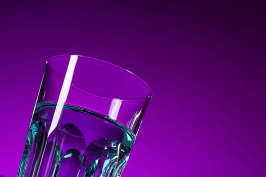 The water in glass on lilac background at studio. Vivid bright colored lighting. Trendy in 2018 Ultra Violet Light Bulb. Art decoration with tone of mystic color