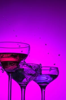 Three wine stuffed glasses standing on the table at studio. Vivid bright colored lighting. Trendy in 2018 Ultra Violet Light Bulb. Art decoration with tone of mystic color
