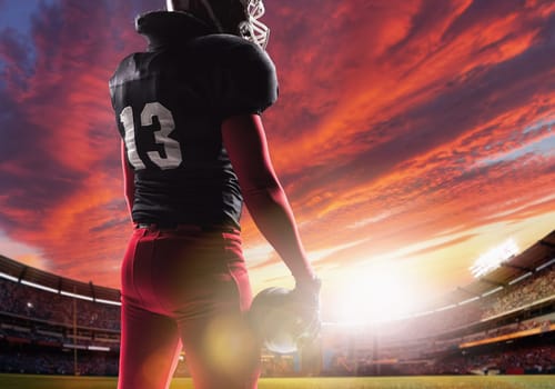 Caucasian fitness man as american football player holding a ball on stadium background at sunset