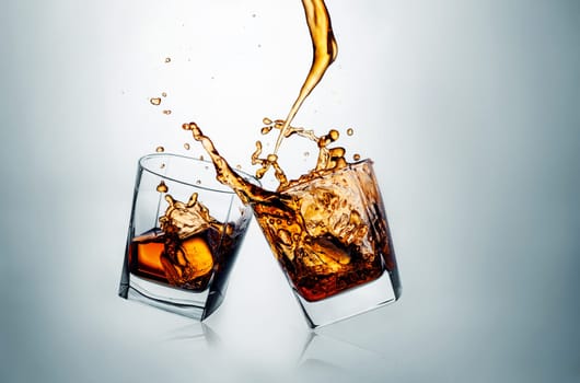 Two whiskey glasses clinking together on gray studio background