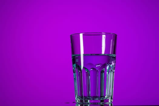 The water in glass on lilac background at studio. Vivid bright colored lighting. Trendy in 2018 Ultra Violet Light Bulb. Art decoration with tone of mystic color