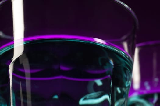 Two wine stuffed glasses standing on the table at studio. Vivid bright colored lighting. Trendy in 2018 Ultra Violet Light Bulb. Art decoration with tone of mystic color
