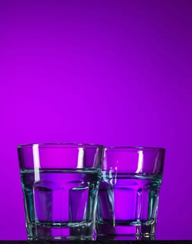 The water in two glasses on lilac background at studio. Vivid bright colored lighting. Trendy in 2018 Ultra Violet Light Bulb. Art decoration with tone of mystic color