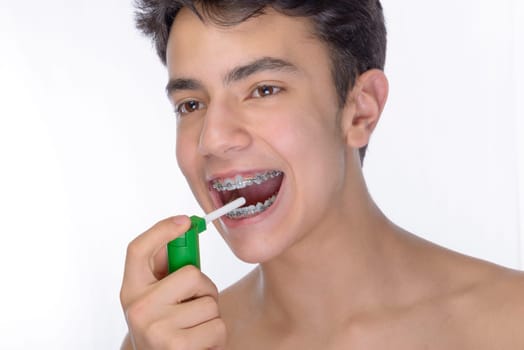 Cute teenager with white background, wearing braces on his teeth. Spray a disinfectant mouthwash in the throat.