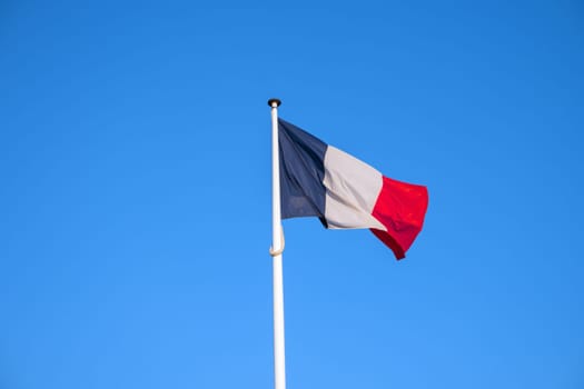 French national official flag on blue sky background. Symbol of France. Patriotic french banner, design. Flag of France on flagpole waving in the wind