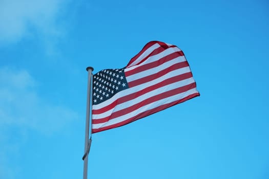 American national official flag on blue sky background. Symbol of the United States. Patriotic US banner, design. Flag of USA on flagpole waving in the wind
