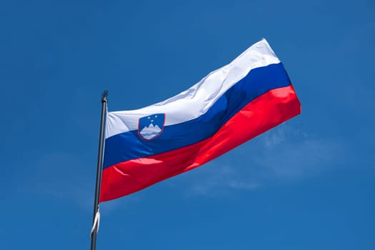 Flag of Slovenia on flagpole waving in the wind. Slovenian national official flag on blue sky background. Patriotic symbol, banner