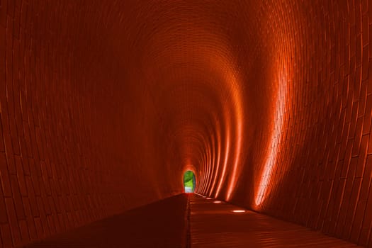 Empty long arched brick pedestrian tunnel, Prague. Orange brick walls, strip of lighting lamp. Bright arch. Underground mysterious footpath for walkers. Underpass and nature at end of tunnel, concept