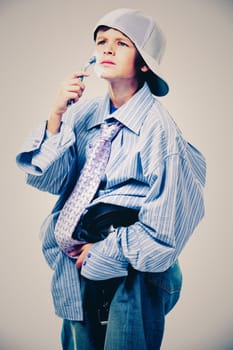 Caucasian boy wearing his Dad's shirt, jeans and tie on light background. He is wearing big adult size clothes which are too big for him.