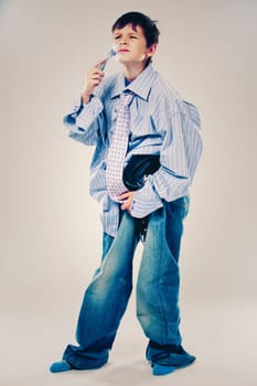Caucasian boy wearing his Dad's shirt, jeans and tie on light background. He is wearing big adult size clothes which are too big for him.