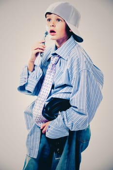 Caucasian boy wearing his Dad's shirt, jeans and tie on light background. He is wearing big adult size clothes which are too big for him.
