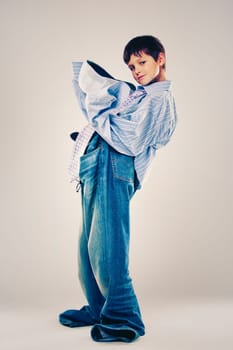 Caucasian boy wearing his Dad's shirt, jeans and tie on light background. He is wearing big adult size clothes which are too big for him.