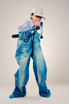 Caucasian boy wearing his Dad's shirt, jeans and tie on light background. He is wearing big adult size clothes which are too big for him.