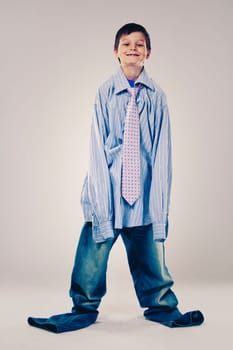 Caucasian boy wearing his Dad's shirt, jeans and tie on light background. He is wearing big adult size clothes which are too big for him.