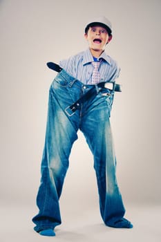 Caucasian boy wearing his Dad's shirt, jeans and tie on light background. He is wearing big adult size clothes which are too big for him.