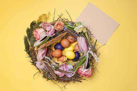 Easter card. Painted Easter eggs in nest on yellow table background. Top view of easter decoration. Happy easter concept