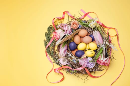 Easter card. Painted Easter eggs in nest on yellow table background. Top view of easter decoration. Happy easter concept