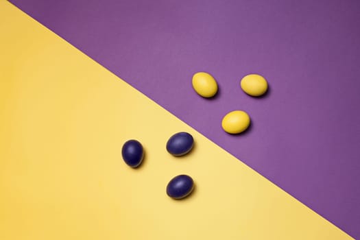 Beautiful easter table setting composition. A row of lilac and yellow color eggs on lviolet and yellow background. Happy Easter greeting card. Top view, copy space.