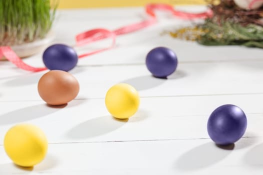 Beautiful easter table setting composition. A row of lilac and yellow color eggs on white wooden table background. Happy Easter greeting card. Side view