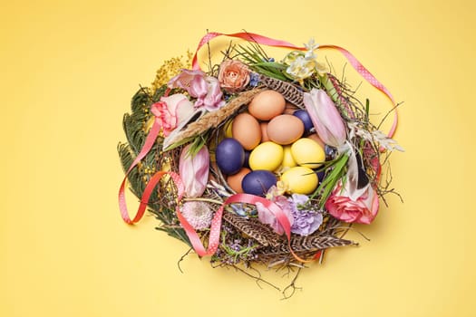 Easter card. Painted Easter eggs in nest on yellow table background. Top view of easter decoration. Happy easter concept