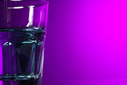 The water in glass on lilac background at studio. Vivid bright colored lighting. Trendy in 2018 Ultra Violet Light Bulb. Art decoration with tone of mystic color